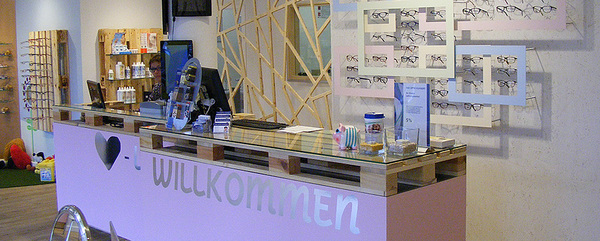 Moderner Optikerladen mit Empfangstresen, Brillenpräsentation und freundlicher Atmosphäre.