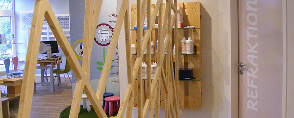 Modern eingerichtetes Optikergeschäft mit Brillenregalen, Sehtestbereich und Pflegemittel-Auslage.